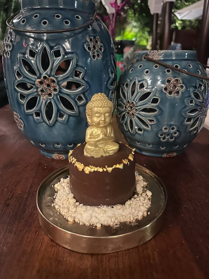 A chocolate birthday dessert topped with a gold buddha