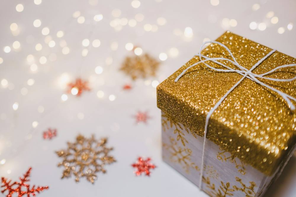 A gold glitter gift box tied with white string, surrounded by sparkly snowflakes