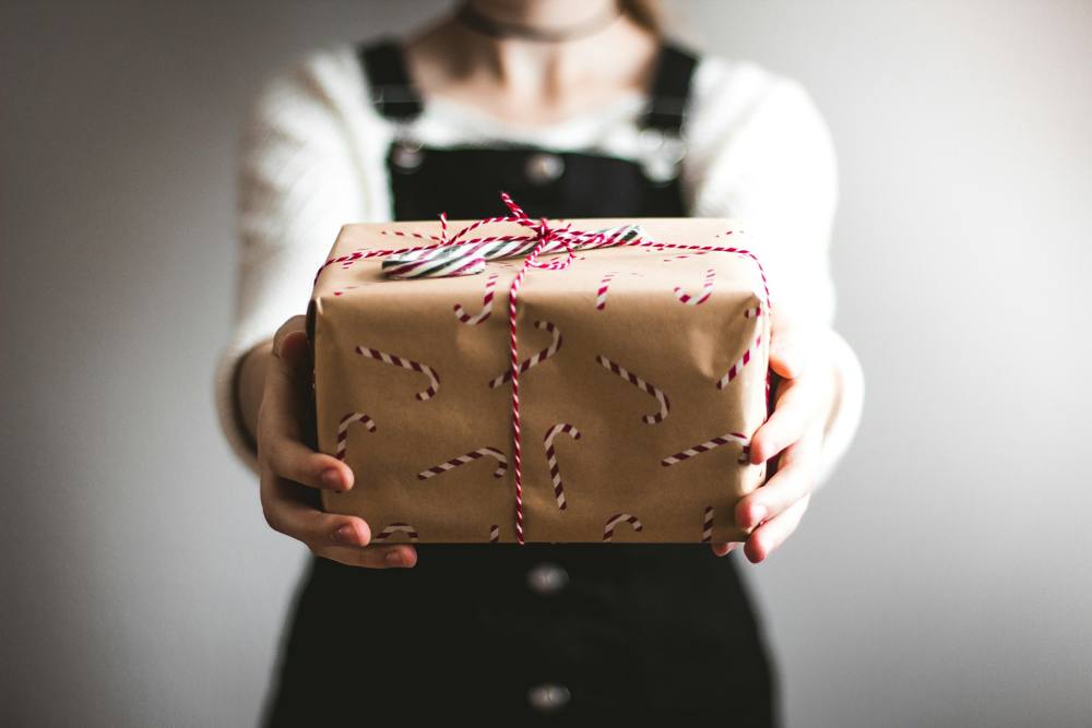 Hands holding out a gift wrapped in candy cane paper and red and white twine