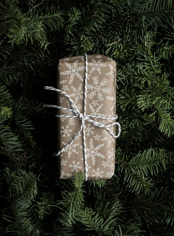 A gift in kraft snowflake paper tied with twine, resting on evergreen branches