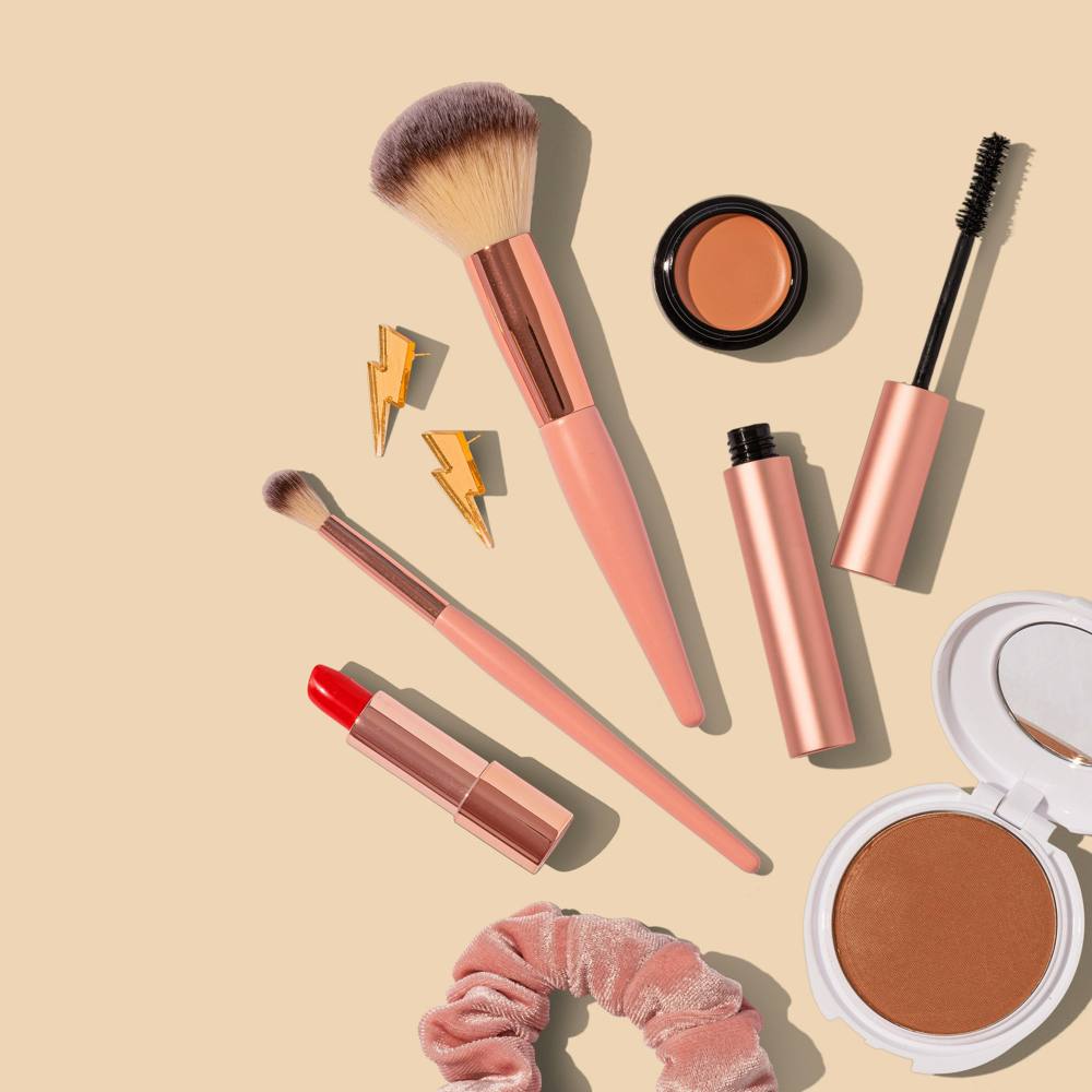 A makeup flat lay with pink brushes and red lipstick