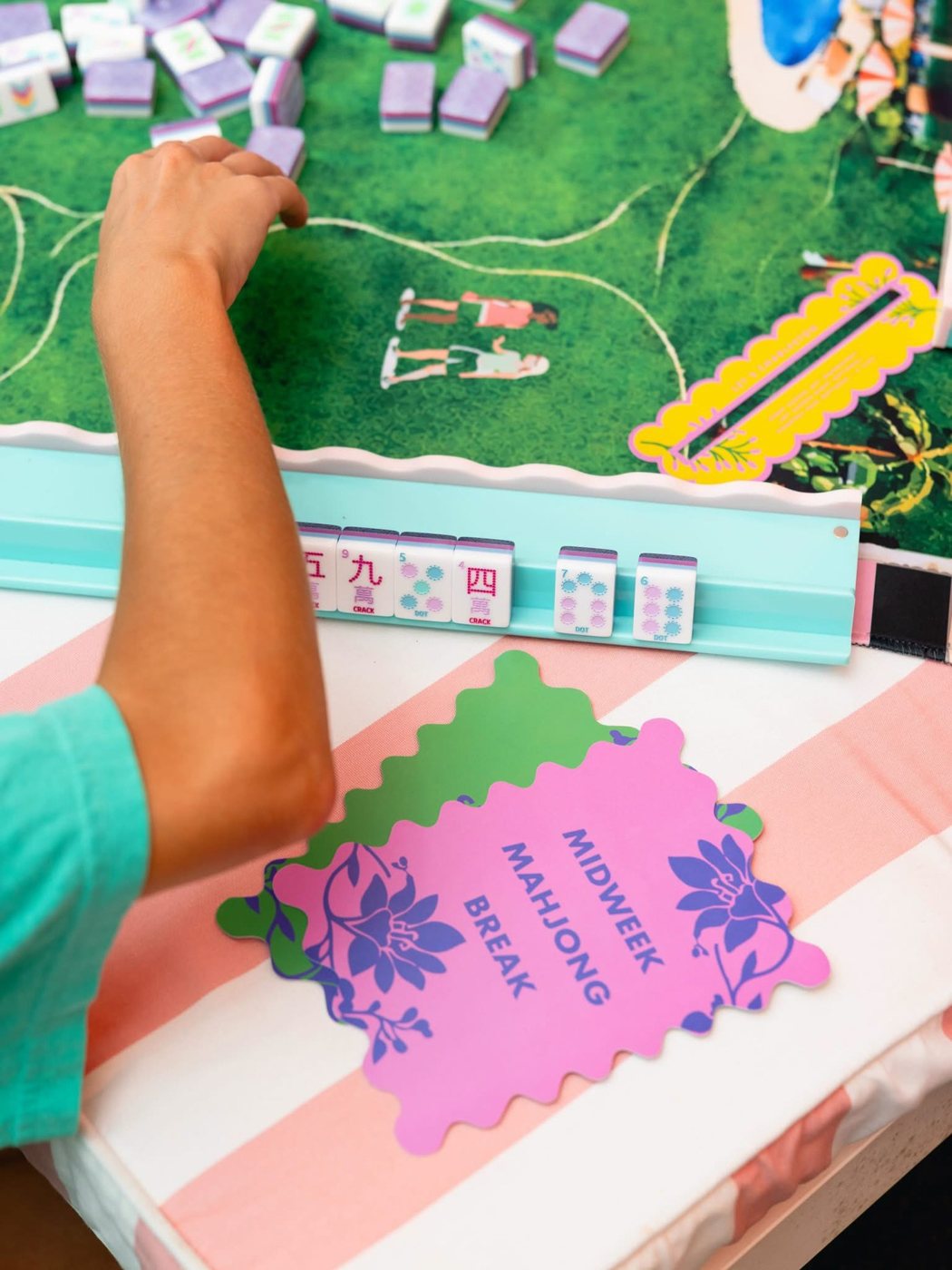 Colorful mahjong tiles on a rack beside a pink Midweek Mahjong Break card