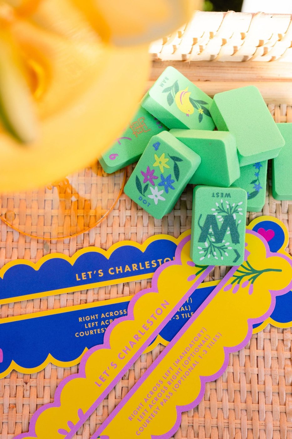 Green floral mahjong tiles on a woven rattan tray beside colorful Let's Charleston reminder cards