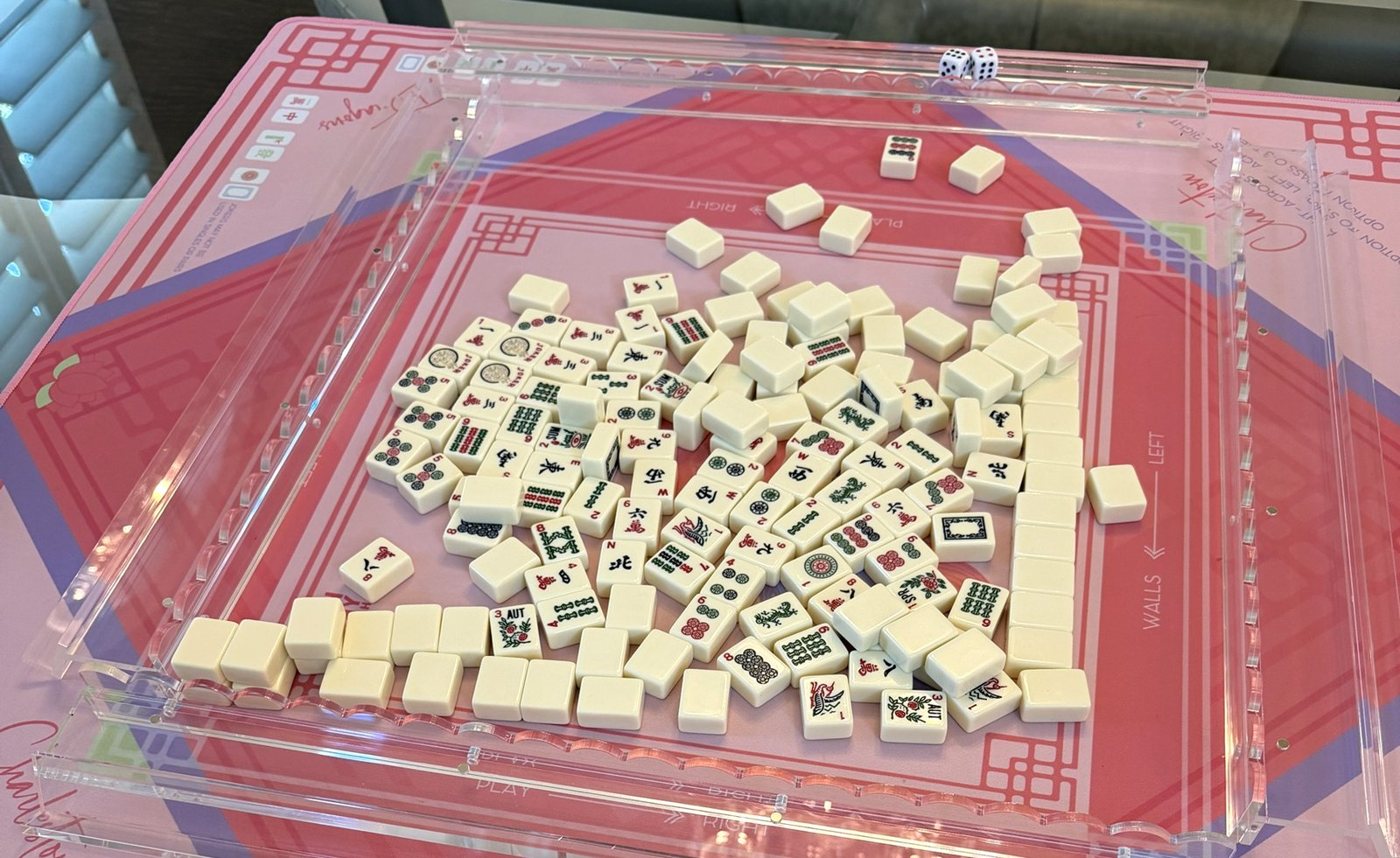 Traditional mahjong tiles mid-game in clear acrylic racks on a pink mahjong mat, with two dice