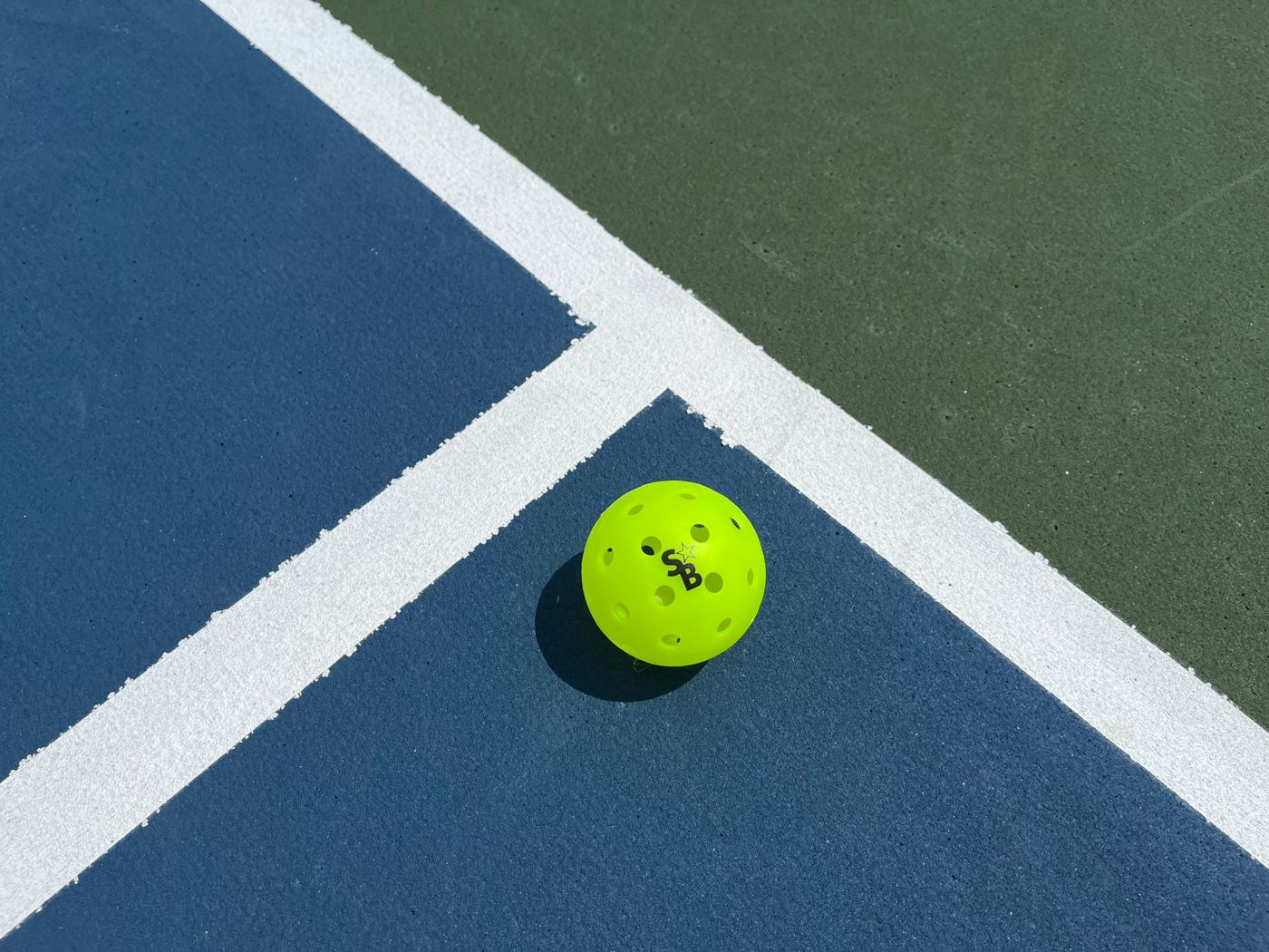 A bright yellow pickleball on a blue and green court